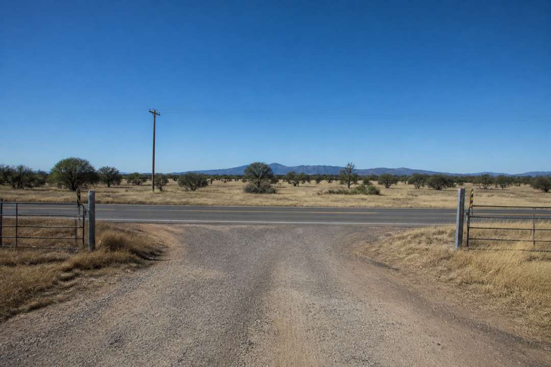Gravel ranch entrance meeting a paved rural road with open land beyond